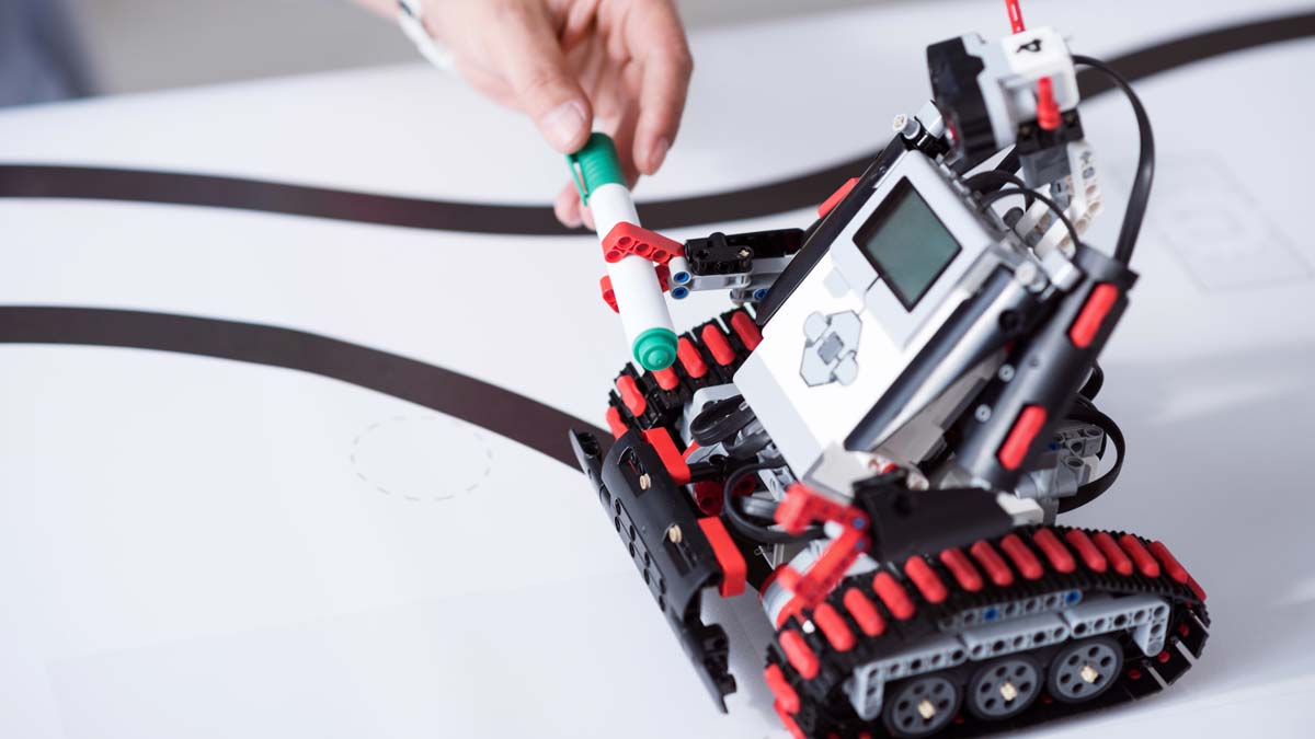 Robot LEGO® Mindstorms mi véhicule mi-humanoïde auquel une main humaine tend un stylo