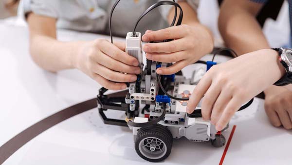 Mains d'adolescents en train de collaborer aux réglages d'un robot sur un tapis spécial